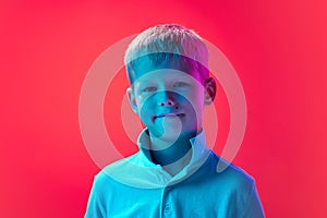 Portrait of little smiling boy, child with short blonde hair posing in white shirt against pink studio background in