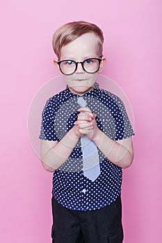 Portrait of a little smiling boy in a funny glasses and tie. School. Preschool. Fashion. Studio portrait over pink background