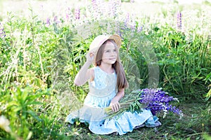 Portrait of little smiling brunette girl with long hair having fun on a stunning blooming meadow of lupines on a golden sunset bac