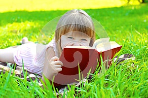 Portrait of little smiling girl child with book lying on grass