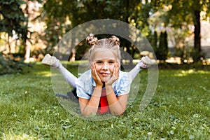 Portrait of a little smiling girl lying on the grass. schoolgirl lies on the grass in the park