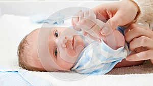 Portrait of little smiling newborn baby lying in crib and holding mother's finger