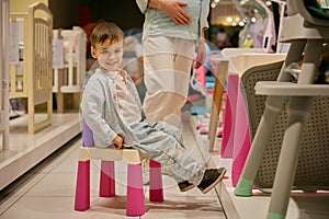 Portrait of little son sitting on chair while mother choosing new furniture