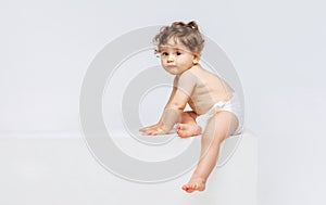 Portrait of little sweet toddler boy, baby in diaper calmly sitting isolated over white studio background