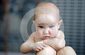 Portrait of little thoughtful baby with big blue eyes. Cute child with short hair, without shirt. Grey background