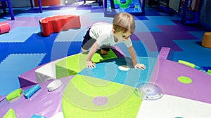 Portrait of little toddler boy crawling and playing on the colorful children palyground covered with soft mats in