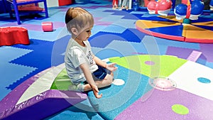 Portrait of little toddler boy crawling and playing on the colorful children palyground covered with soft mats in photo