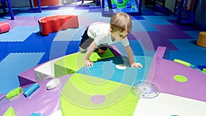 Portrait of little toddler boy crawling and playing on the colorful children palyground covered with soft mats in photo