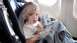 Portrait of little toddler boy sitting in airplane and eating croissant