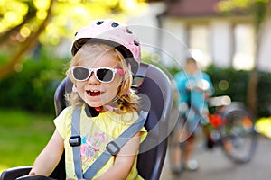 Portrait of little toddler girl with security helmet on the head sitting in bike seat of parents. Boy on bicycle on