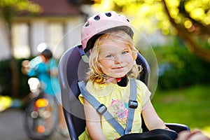 Portrait of little toddler girl with security helmet on the head sitting in bike seat of parents. Boy on bicycle on