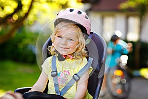 Portrait of little toddler girl with security helmet on the head sitting in bike seat of parents. Boy on bicycle on