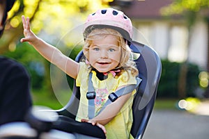 Portrait of little toddler girl with security helmet on the head sitting in bike seat of parents. Boy on bicycle on