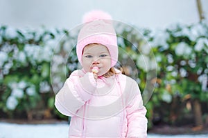 Portrait of little toddler girl walking outdoors in winter. Cute toddler eating sweet lollypop candy. Child having fun