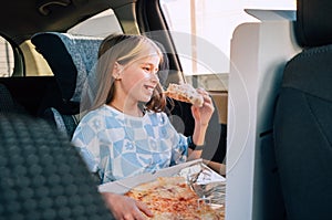 Portrait of little 5 YO girl eating just cooked Italian pizza sitting in child car seat on car back seat and looking out window .