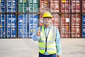 Portrait of Logistic engineer worker man standing in shipping container yard looking and thumb up to the camera. Confident