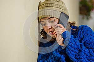 Portrait of lonely homeless woman on the street in cold autumn weather wearing a blue hoodie and using her cellphone at