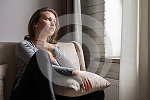 Portrait of lonely sad Ñaucasian young woman sitting near window of apartments.