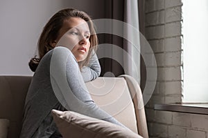 Portrait of lonely sad Ñaucasian young woman sitting near window of apartments.