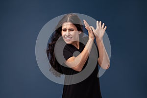 Portrait of a long-haired brunette woman in black t-shirt posing on a gray background and showing different emotions.