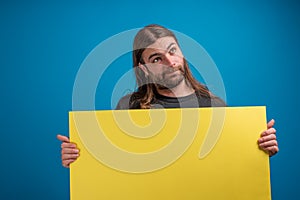 Portrait of long haired male looking away from camera and holding a yellow banner for advertise.