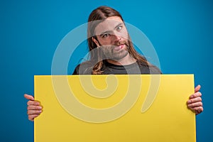 Portrait of long haired male looking away from camera and holding a yellow banner for advertise while displaying a
