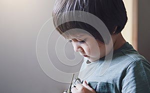 Portrait of lonly kid boy with sad face playing alone, Bored Child looking at tank toy with thinking face