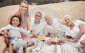 Portrait, love and happy interracial family having a picnic on the beach and smile while having some food with snacks