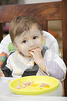 Portrait of lovely baby at table with hand in mouth