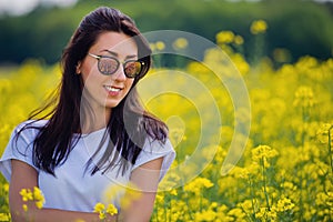 Portrait of lovely brunette in sunglasses stay in rapeseed field. Spring.