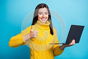 Portrait of lovely cheerful girl holding in hands laptop showing thumbup advert isolated over bright blue color