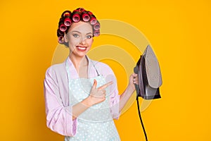 Portrait of lovely cheery maid holding in hand demonstrating new modern iron steam isolated bright orange color