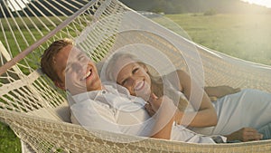 PORTRAIT: Lovely couple reclining in hammock laughs in beautiful summer nature.