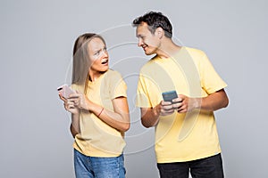 Portrait of lovely couple with smart phones in hands, cheerful charming woman checking her email, man follows her secret