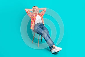 Portrait of lovely cute senior woman wear checkered trendy clothes sit chair isolated on cyan color background