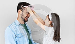 Portrait of lovely daughter smiling broadly puts the princess`s crown on the head of her handsome father isolated over light gray