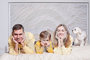 Portrait of lovely family, friendly parents, mom and dad with adorable child son and white dog on the bed