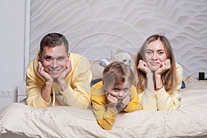 Portrait of lovely family, friendly parents, mom and dad with adorable child son and white dog laiyng on the bed