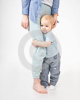 Portrait of lovely family standing on white background. Cherubic little blond girl baby daughter embracing mothers leg.