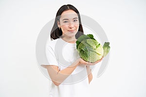 Portrait of lovely korean woman, showing cabbage, holding lettuce green vegetable and smiling, isolated on white