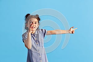 Portrait of lovely little girl, child with curly hair and cute hairdo posing against blue studio background. Whispering