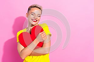 Portrait of lovely nice positive girl closed eyes arms hold hug paper heart symbol card empty space isolated on pink