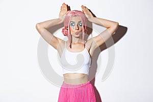 Portrait of lovely party girl in pink anime wig, showing bunny ears and pouting silly, celebrating halloween, standing