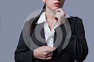Portrait of a lovely young business lady in a business suit. Girl succinctly holds her hands to her face. On a gray background. photo