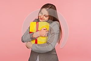 Portrait of lovely young businesswoman in suit jacket embracing gift box tightly and smiling with happiness photo