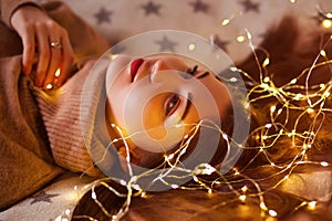 Portrait of a lovely young women, lying on a bed with garlands. Merry Christmas and Happy New Year