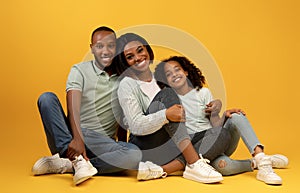 Portrait of loving black parents and their cute daughter smiling together to camera over yellow background