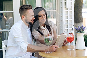 Portrait of a loving couple sitting in a cafe. A man and a woman spend time together, watch something on the tablet