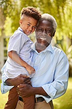 Portrait Of Loving Grandfather Holding Grandson In Arms In Garden At Home