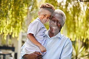 Portrait Of Loving Grandfather Holding Grandson In Arms In Garden At Home